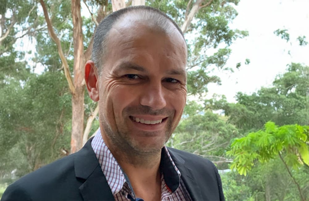 Headshot of man outdoors with trees in background.
