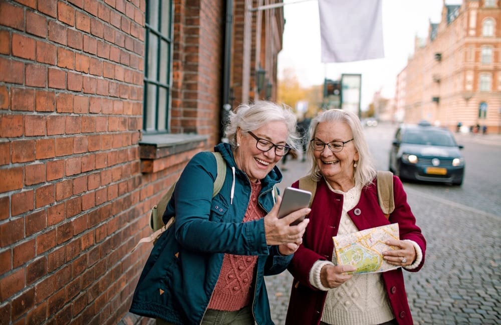 Two mature female travellers with map and mobile phone on city street – phone theft.