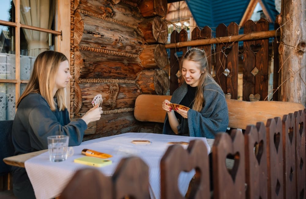 Two female triends playing cards in a log cabin – soft-reset trip concept. Image: Shutterstock